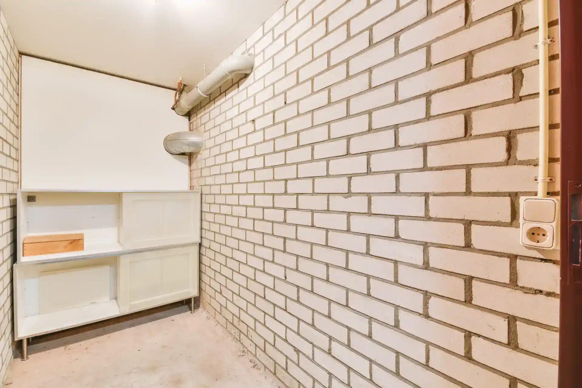 Betonvæg med synlige mursten og gulvbelægning, indendørs rum.