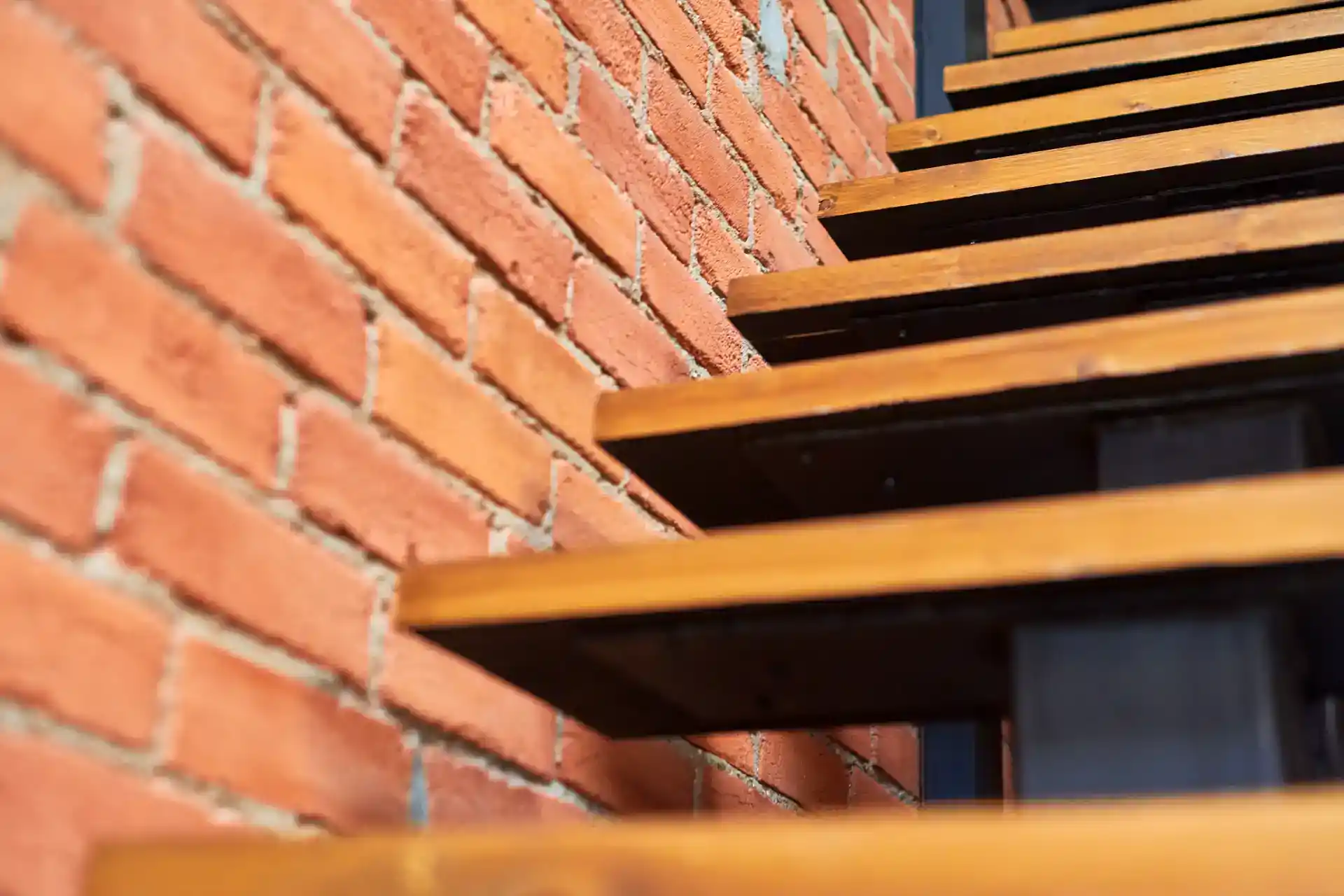 Håndlavede trappesteg i træ foran rødt murstensvæg.