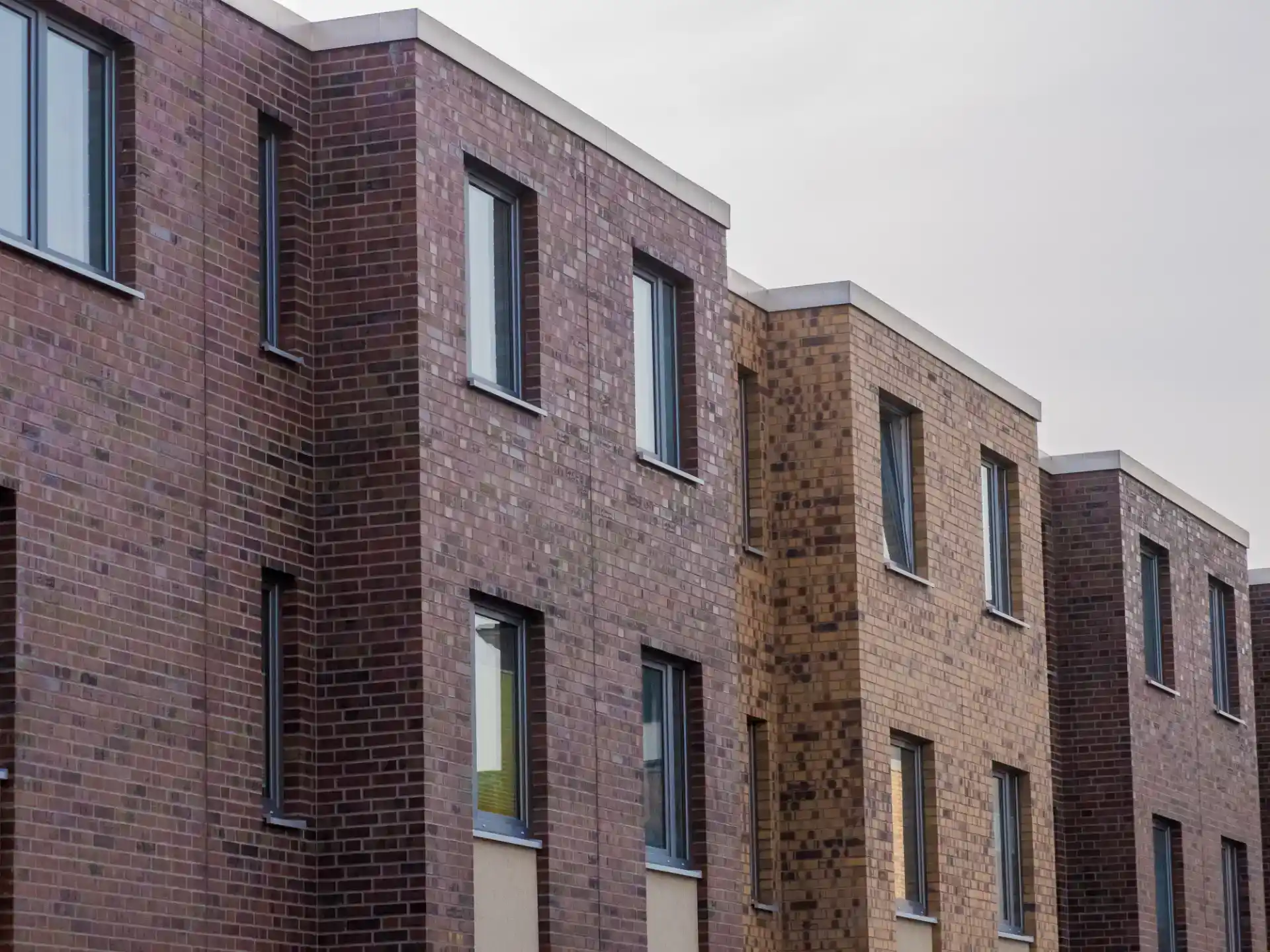 Moderne murstensbygget boligbygning med store vinduer og variation i brickefarver, ideel til bolig- og erhvervsprojekter.