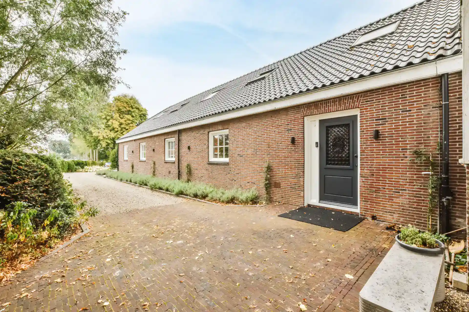 Rustikt rødt murstensejendom med sort dør, boligudlejning og charmerende haveområde.